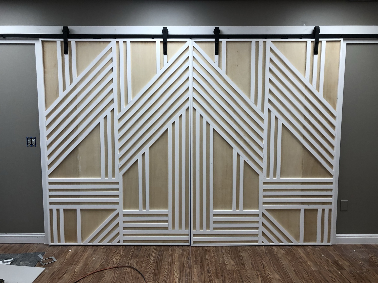 Installed sliding doors with a symmetrical white geometric trim pattern on pale wood panels